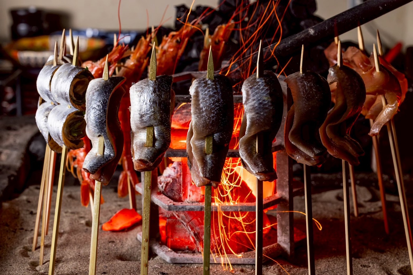 炭火で串焼きの魚介を仕上げる様子